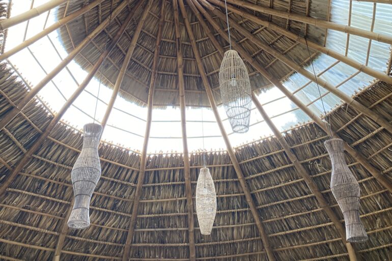 looking up at open roof ceiling with woven light fixtures on bamboo and banana leaf hut